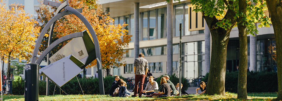 Personen sitzen im Herbst auf der Wiese vor der Bibliothek der Uni Magdeburg (c) Jana Dünnhaupt Uni Magdeburg
