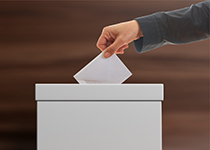 Mann steckt Wahlzettel in eine Wahlurne Mann steckt Wahlzettel in eine Wahlurne