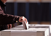 Hand steckt Zettel in Wahlurne Hand steckt Zettel in Wahlurne