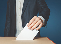 Mann steckt Wahlzettel in eine Wahlurne
